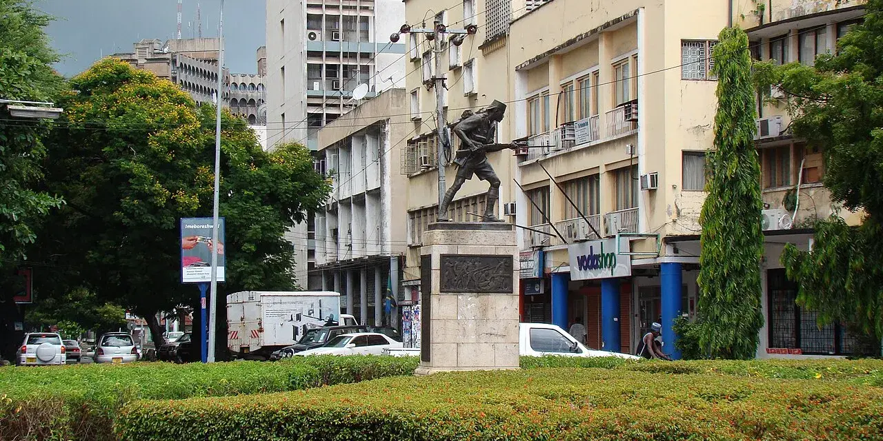 Pomnik żołnierza na tle budynków w Dar es Salaam. W tle widać ruch uliczny i drzewa.