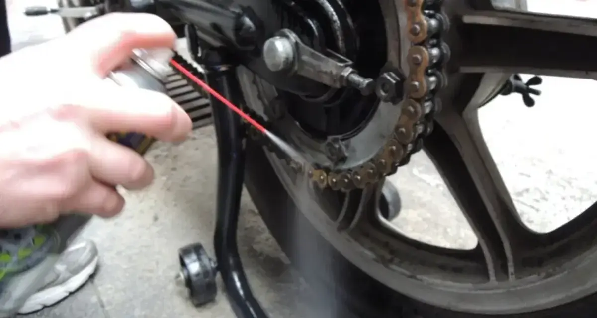 Mano spruzza lubrificante sulla catena della moto. Per sapere ogni quanto ingrassare catena moto, controlla il manuale.