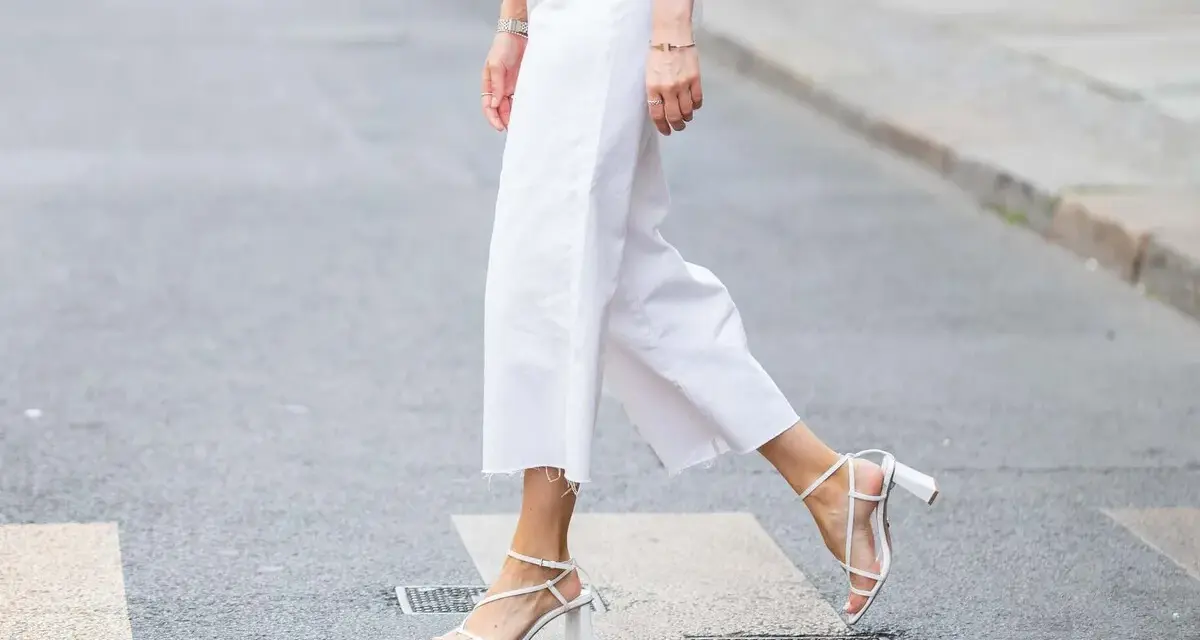Mujer cruza la calle con un look comunión: pantalón blanco de corte ancho y sandalias de tiras.