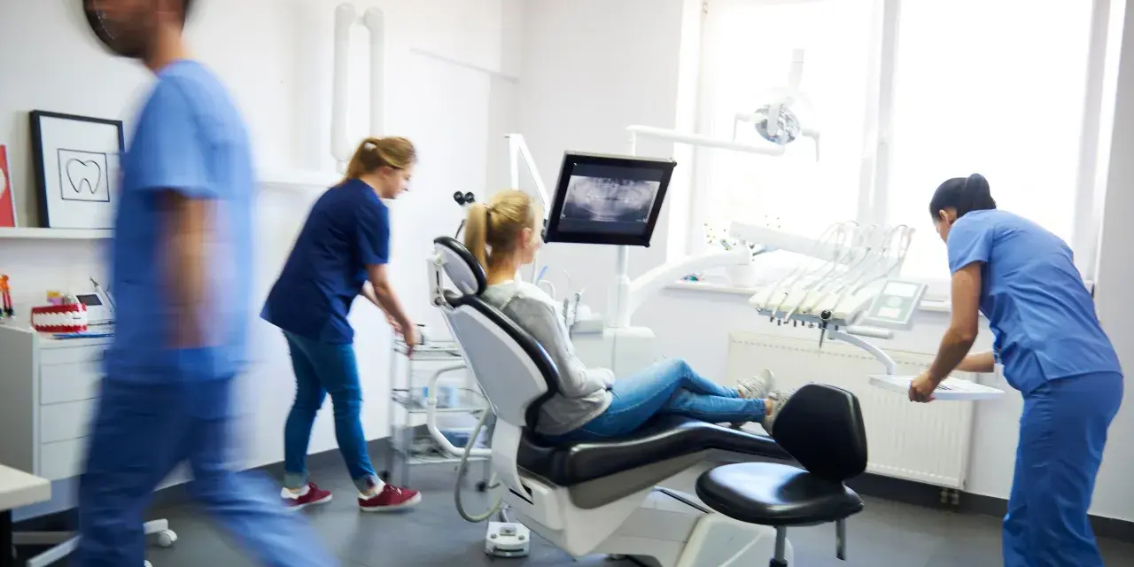 Pacjentka na fotelu dentystycznym, gdzie można wykonać leczenie kanałowe NFZ. Personel przygotowuje narzędzia.