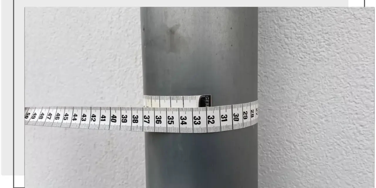 Miarka krawiecka owinięta wokół szarej rury pokazuje, jak zmierzyć średnicę rury. Odczyt wynosi około 32 cm.