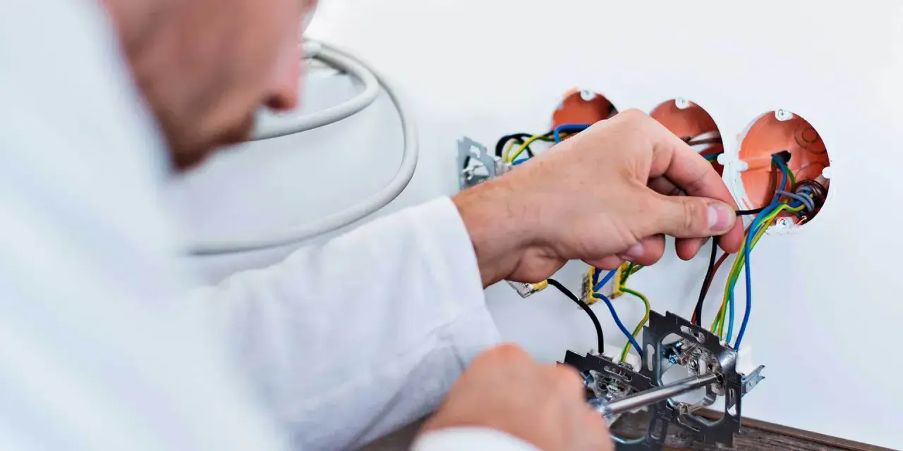 Elektryk dokonuje wymiany instalacji elektrycznej, podłączając przewody do puszek.