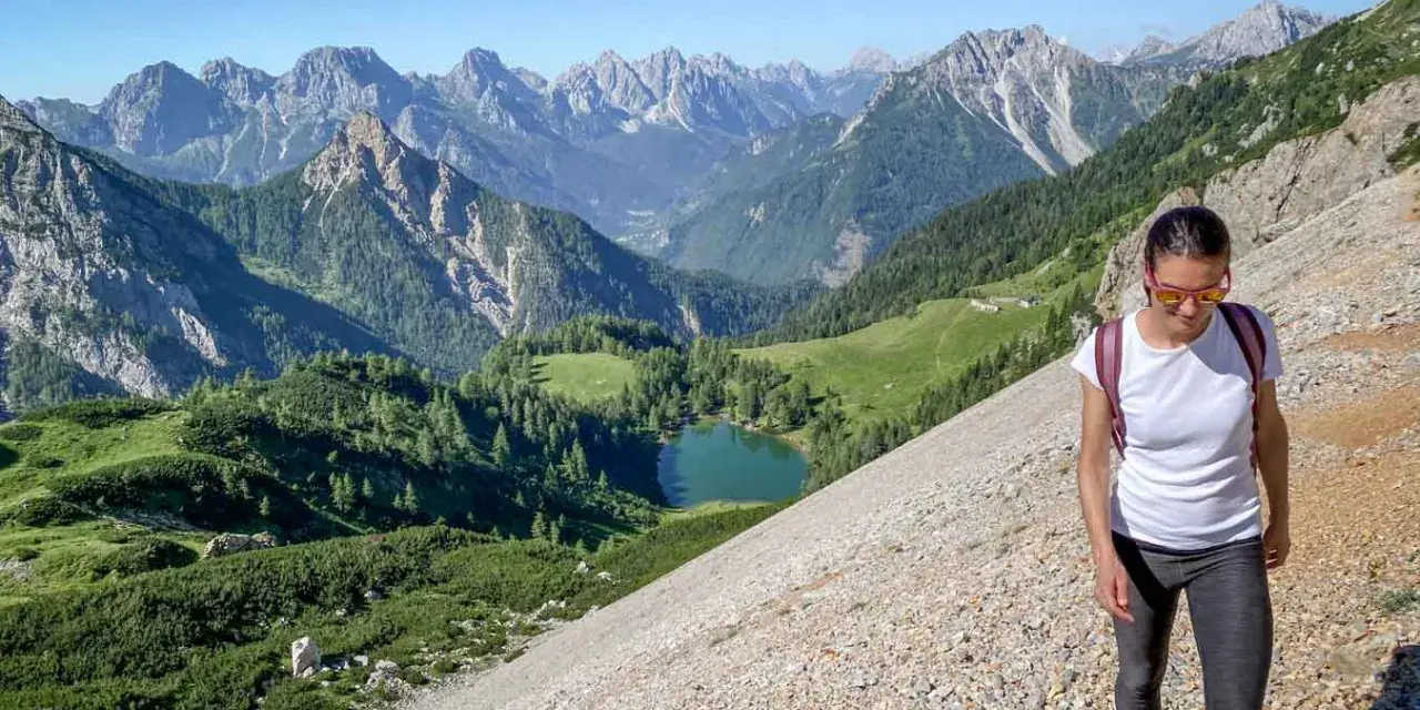 Una donna fa una camminata outdoor in montagna, godendosi il panorama di un lago alpino e vette maestose. Il vero significato di camminata outdoor è qui.