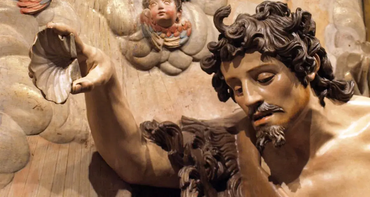 Detalle de escultura barroca: figura masculina con barba y cabello rizado sostiene una concha. Ángeles infantiles observan. Maestría de escultores del barroco.