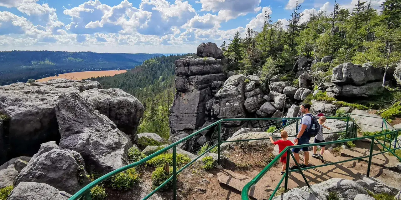 Rodzina wędruje po skalistej trasie Szczeliniec Wielki. Widok na dolinę i chmury.
