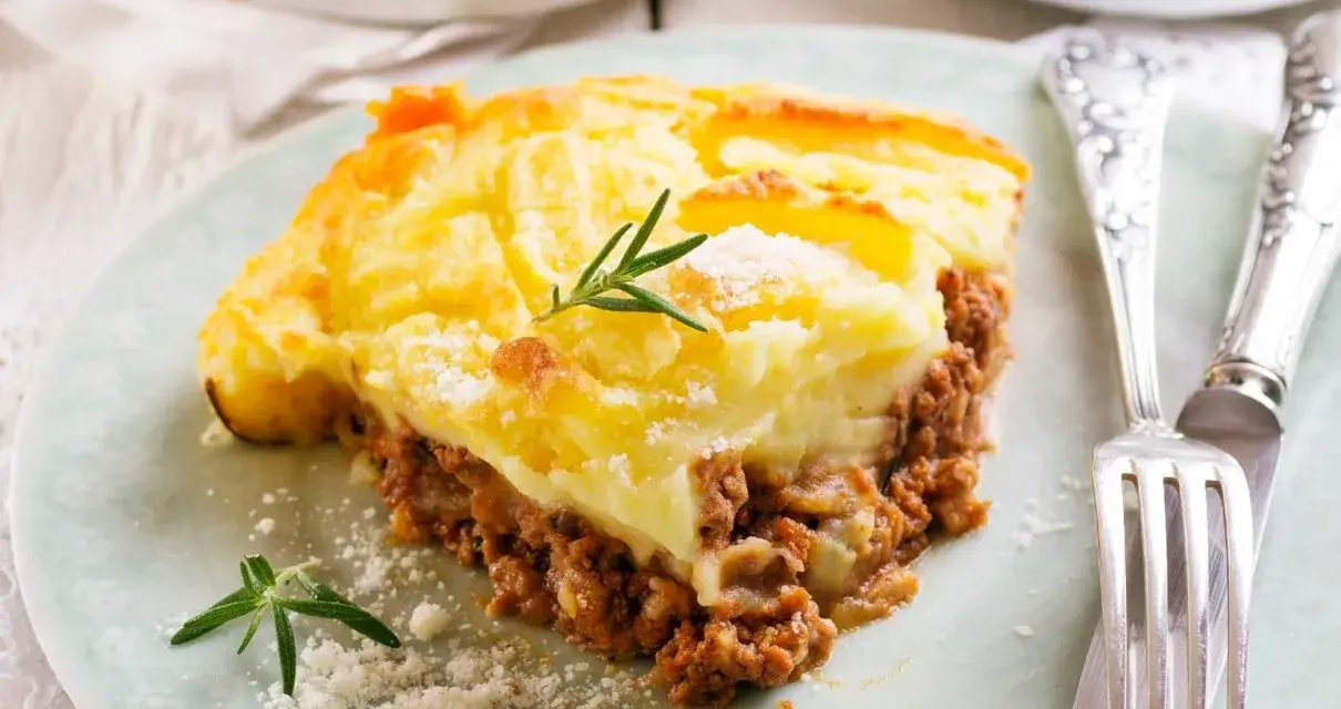 Pyszna zapiekanka pasterska (Shepherd's Pie) z warstwą mielonego mięsa i kremowym purée ziemniaczanym, ozdobiona gałązką rozmarynu.