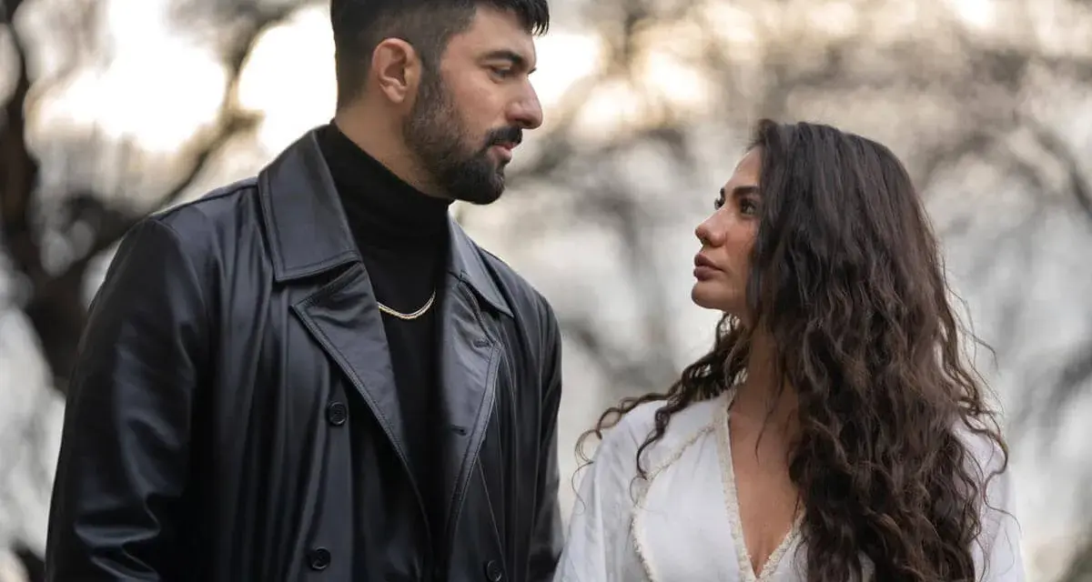 Un uomo con trench di pelle nera e una donna con lunghi capelli scuri si guardano intensamente. Io sono Farah, e questo sguardo dice tutto.