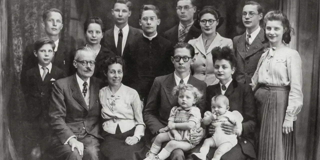 Gros plan sur une famille nombreuse posant pour une photo. On peut y voir des enfants, des adultes et des bébés. Une recherche sur Geneanet pourrait révéler leur nom de famille.