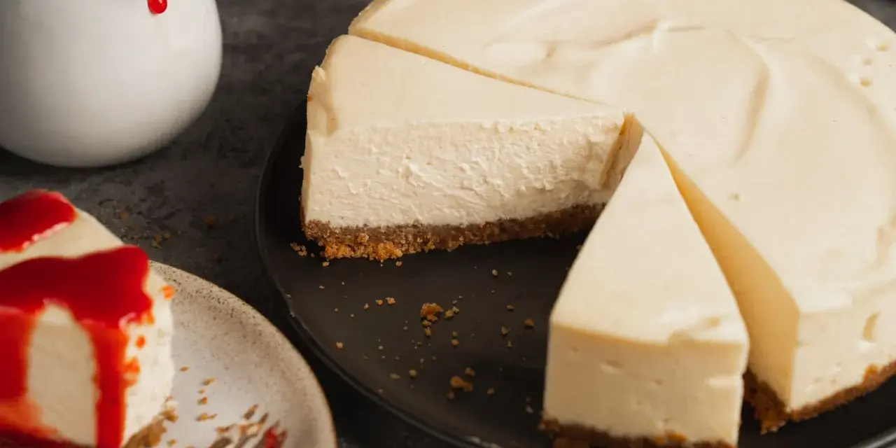 Ein cremiger New York Cheesecake, das Original-Rezept, mit einem Stück auf einem Teller, beträufelt mit roter Soße.