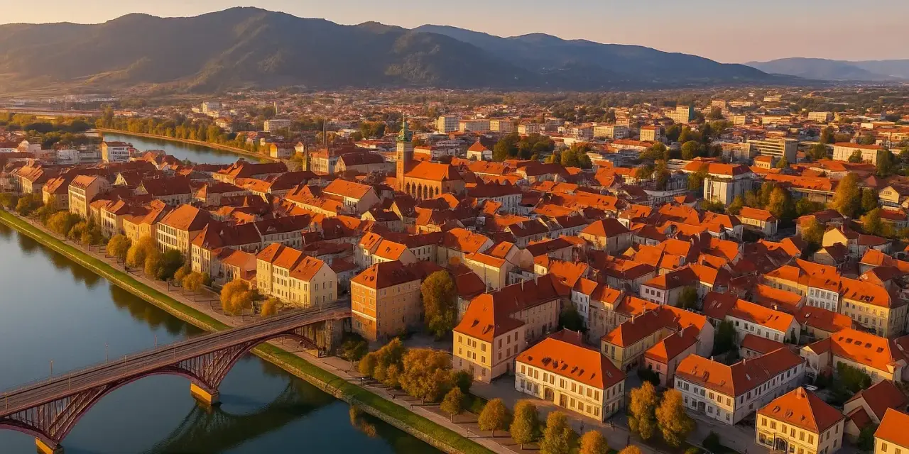 Widok na Maribor z lotu ptaka: rzeka Drava, most, zabytkowe kamienice z czerwonymi dachami i wzgórza w tle. Odkryj mariborskie atrakcje!