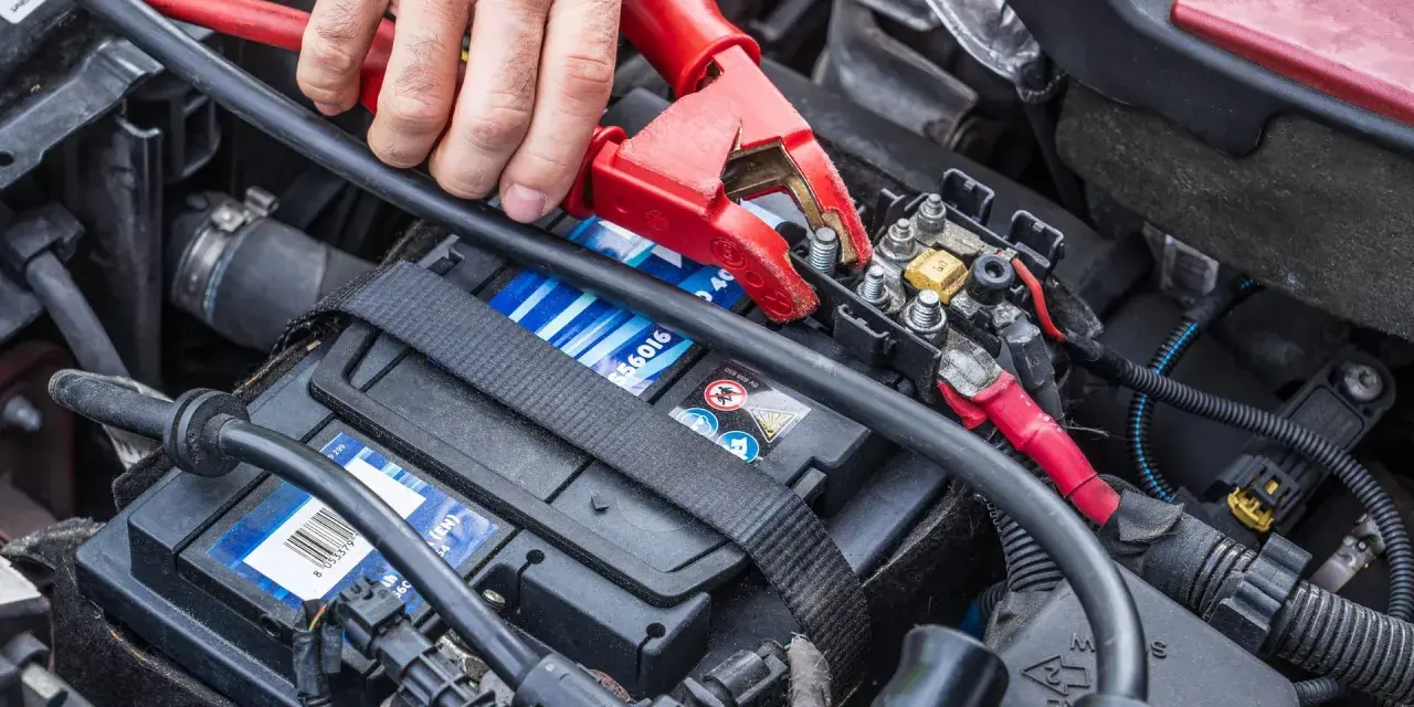 Starthilfe war zuerst: Eine Hand befestigt eine rote Klemme an der Autobatterie, um dem Fahrzeug wieder Leben einzuhauchen.