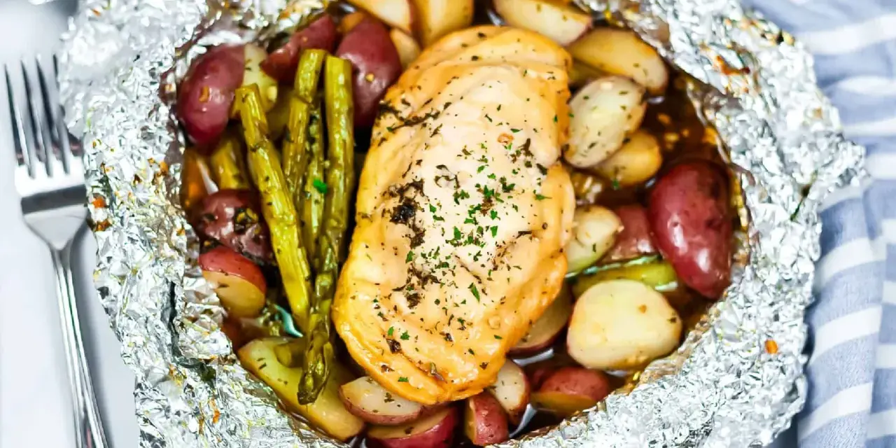 Campfire chicken foil packets in oven, with roasted potatoes and asparagus, seasoned with herbs.