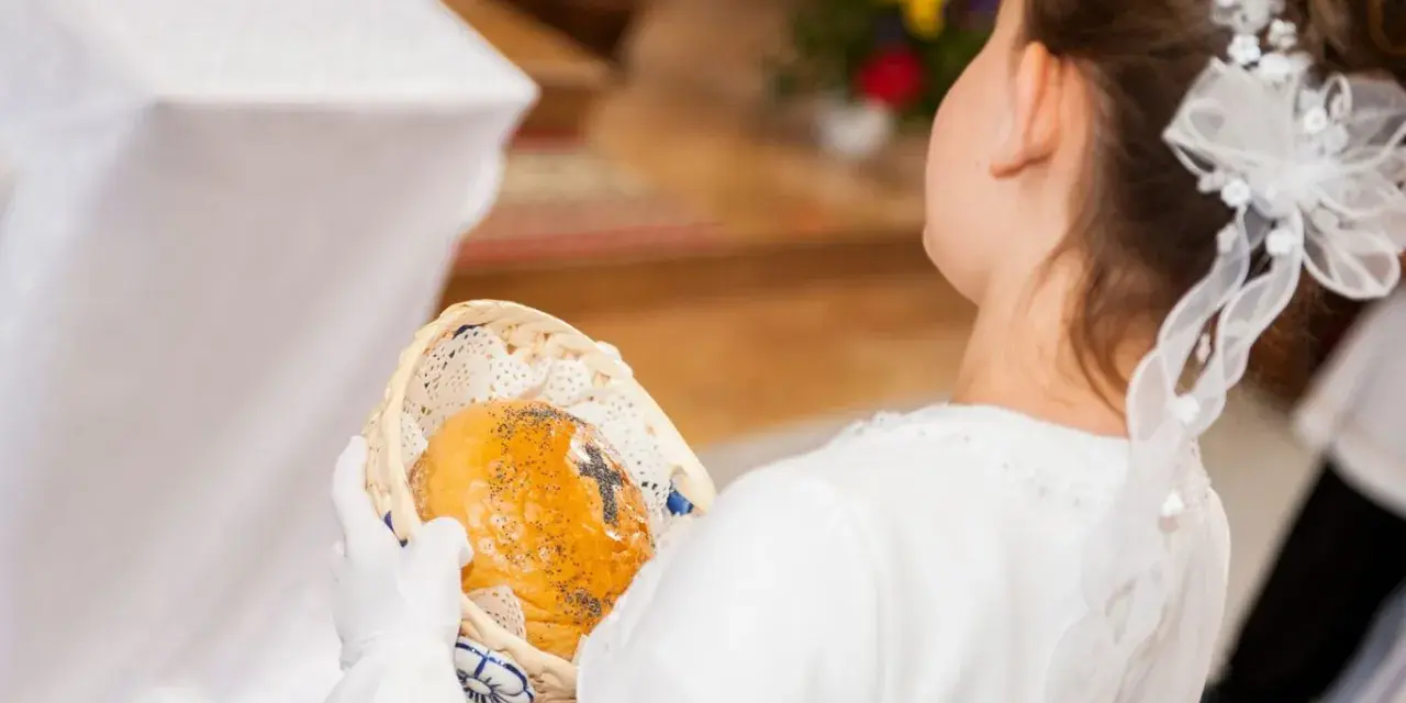 Dziewczynka w bieli trzyma koszyczek z opłatkiem. Zastanawiasz się, ile daje chrzestny na komunię?