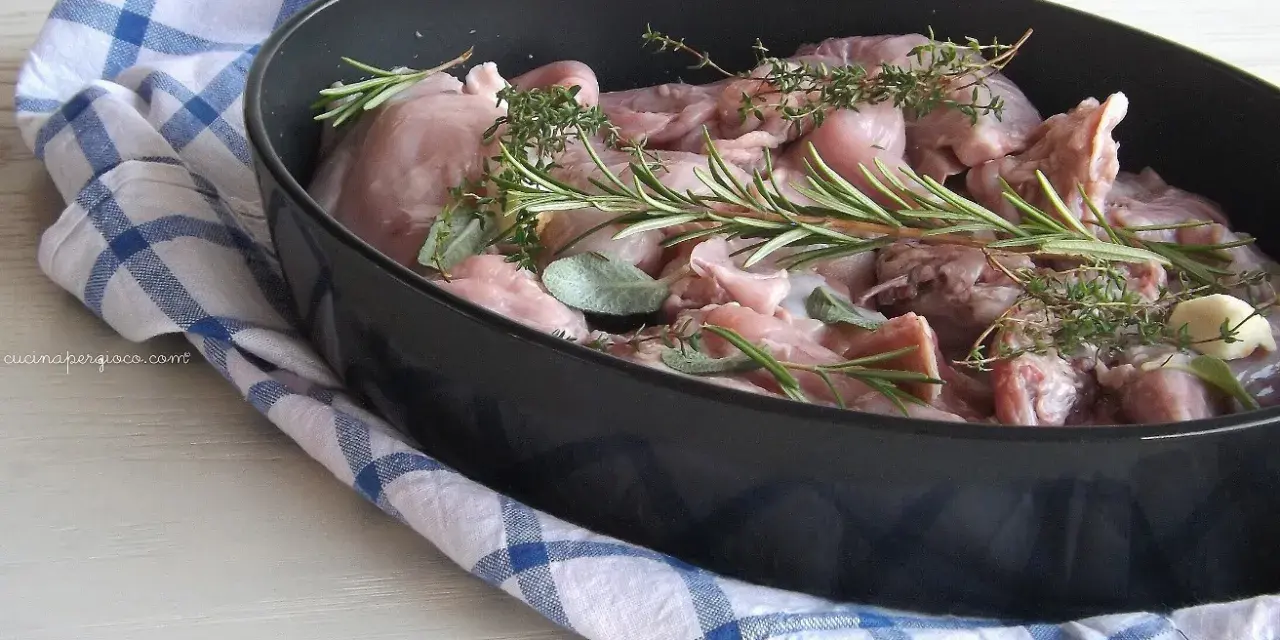 Pezzi di coniglio crudo pronti per essere cucinati al forno, profumati con rosmarino, salvia e aglio.