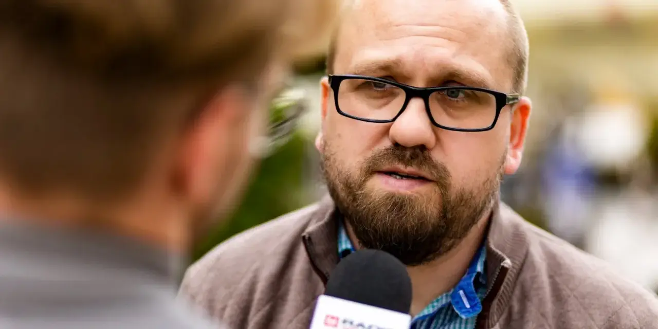 Mężczyzna w okularach udziela wywiadu mikrofonowi radiowemu.