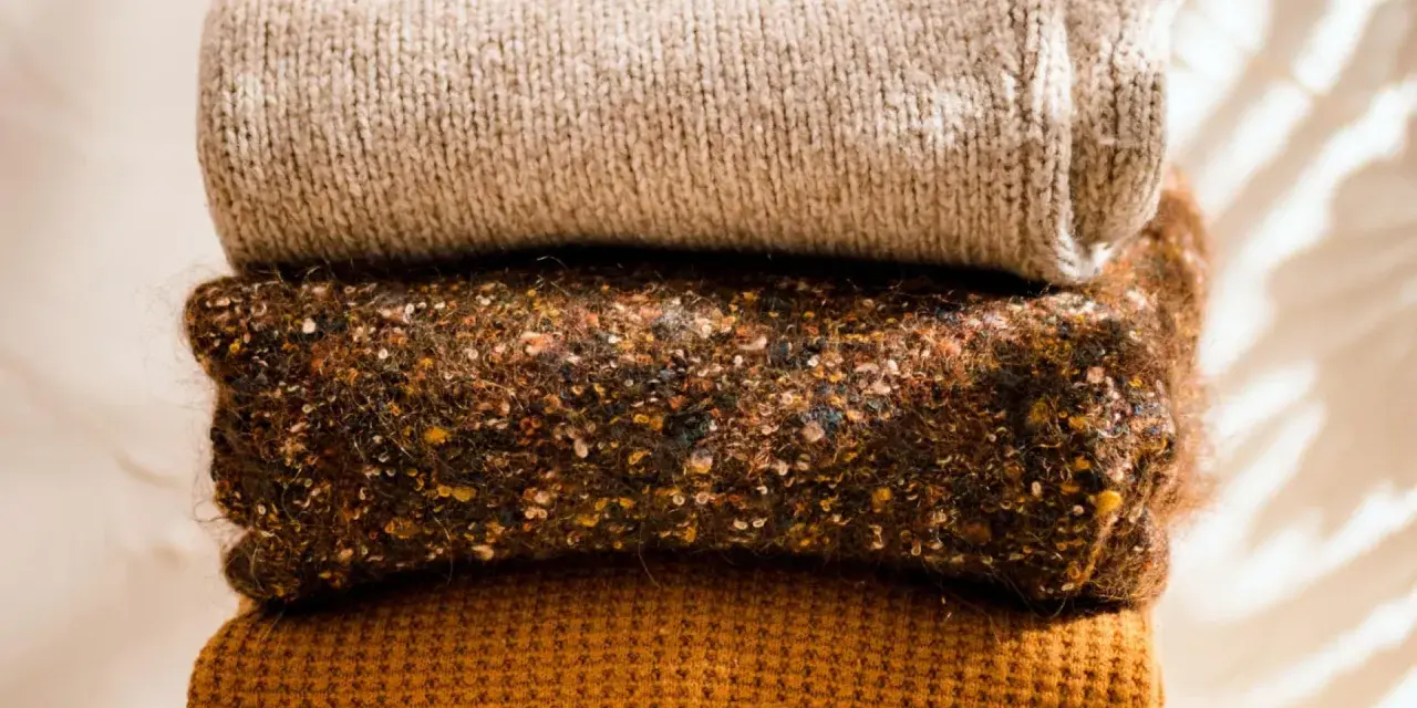 Gestapelte Strickwaren in warmen Herbstfarben. Damit die **Wolle bei 40 Grad waschen** gelingt, sind diese Pullover perfekt.