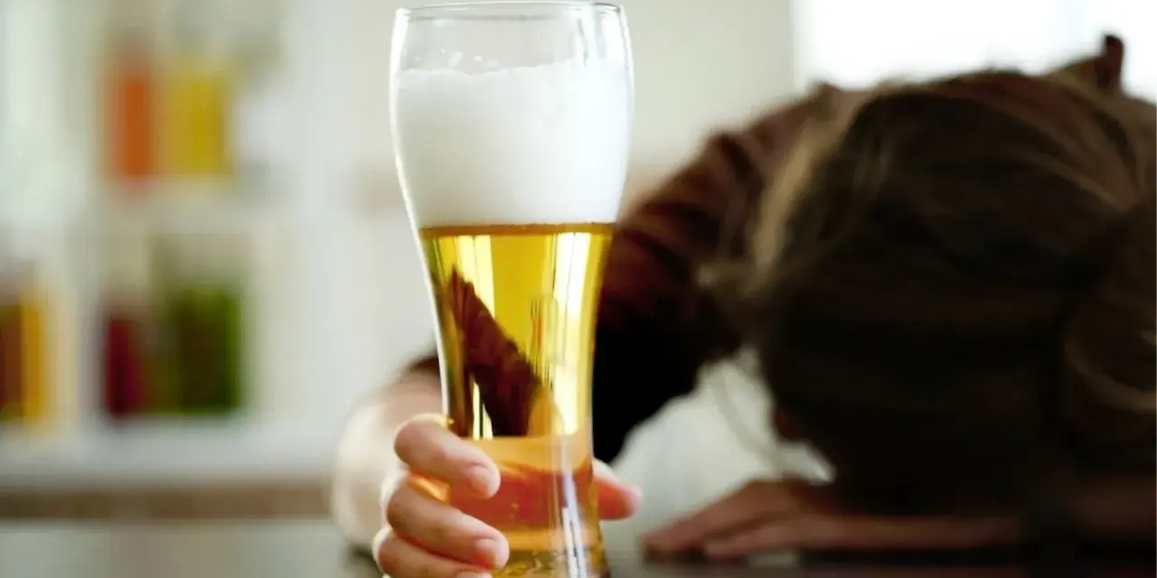 Ręka trzymająca piwo, obok kluczyki samochodowe. Osoba w tle pochylona.