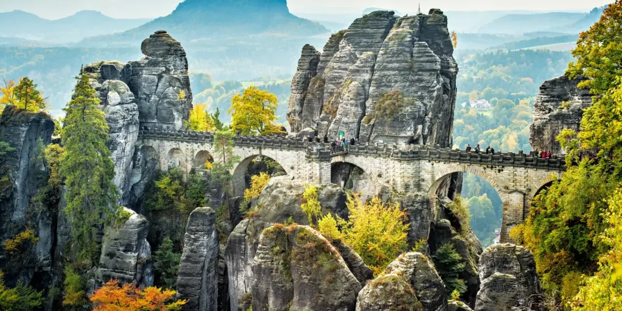 Most Bastei, skalne miasto w Saksonii, z kamiennym mostem łączącym skalne iglice. Jesienne liście dodają koloru krajobrazowi.