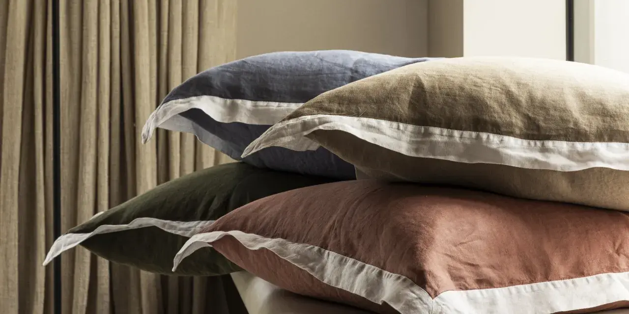 Pile de coussins aux couleurs douces, bleu, kaki, ocre, avec bordure blanche. Le percale de coton, c'est quoi ? Une matière douce et respirante.