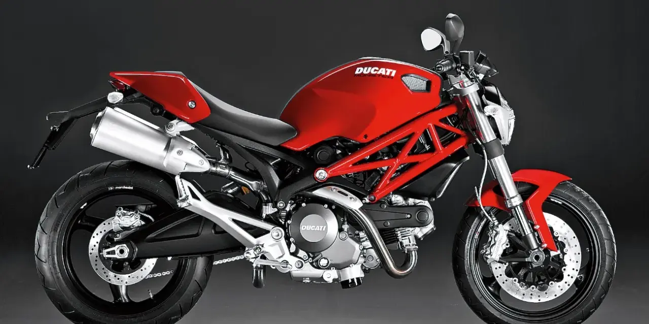 Czerwony Ducati Monster 696 z charakterystyczną kratownicową ramą, błyszczącym wydechem i sportowym siedzeniem.