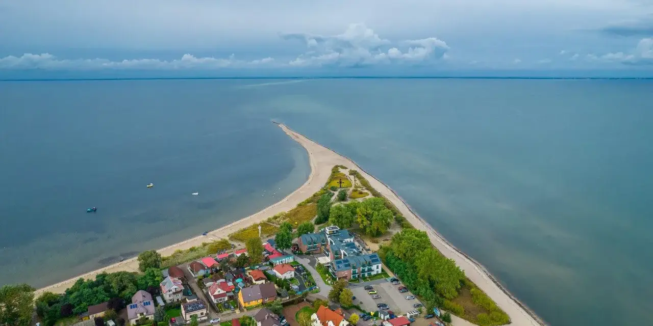 Malownicza miejscowość nad morzem, z domkami i plażą, wcinająca się w spokojne wody.