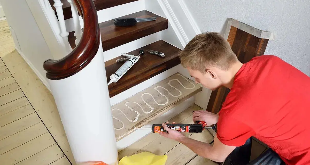 Man lägger lim på en trappsteg för att lägga nytt golv. Trappa inomhus inspiration för ett modernt hem.