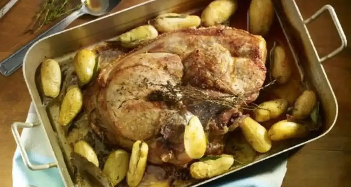 Rouelle de porc rôtie au four, entourée de pommes de terre dorées et d'herbes aromatiques. Un plat savoureux prêt à être dégusté.