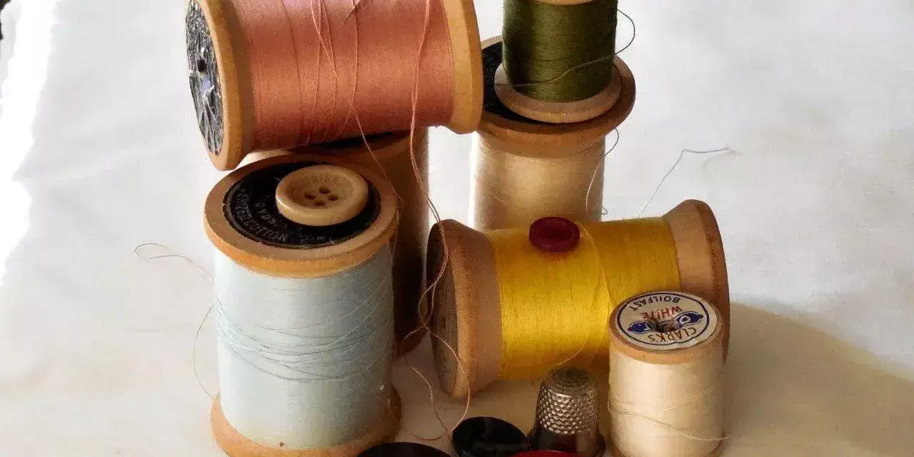 Bobine di filo colorato, bottoni e un ditale, pronti per un punto sopraggitto a mano.