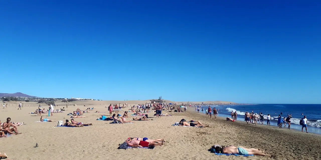 Tłum ludzi odpoczywa na słonecznej plaży. Woda jest spokojna, a niebo bezchmurne. Czy Gran Canaria jest bezpieczna? Tak, wygląda na to, że turyści czują się tu swobodnie.
