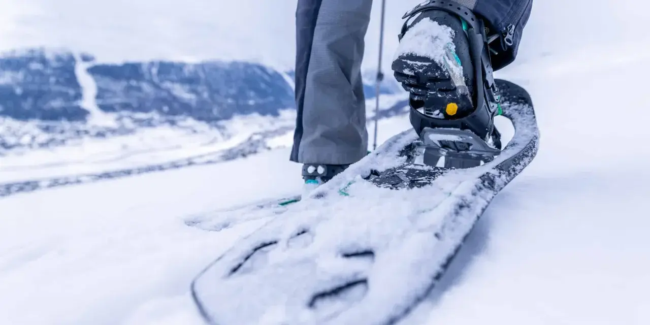Piede con racchette da neve che affonda nella neve fresca, pronto per camminare in montagna.