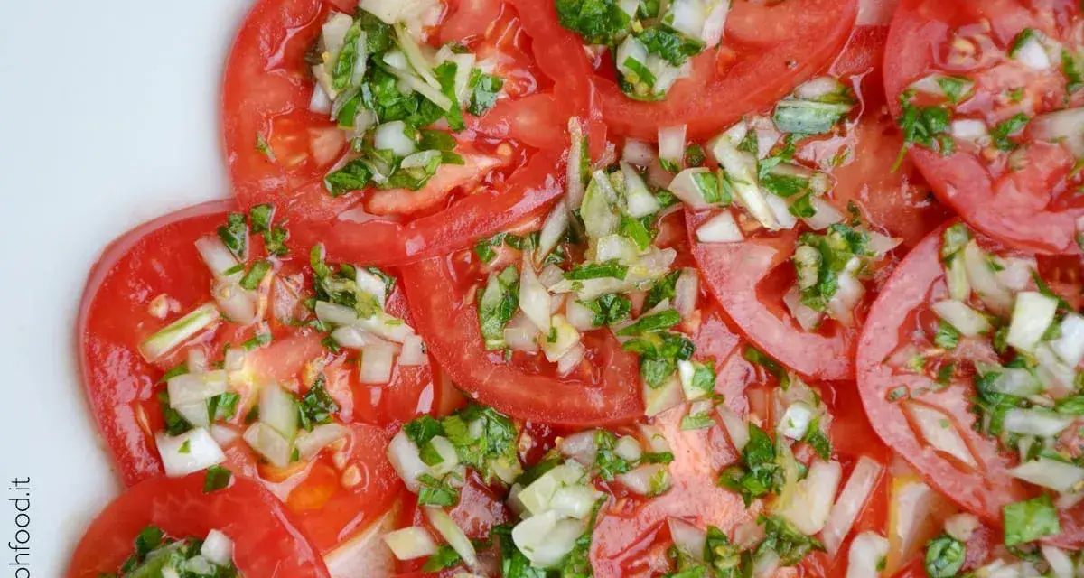 Fette di pomodoro fresco condite con cipolla tritata e erbe aromatiche. Un'insalata di pomodori semplice e gustosa.