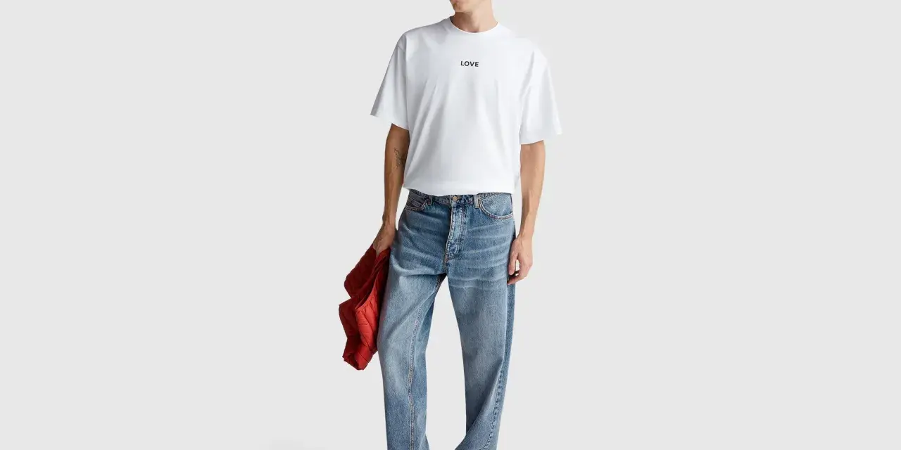 Uomo con t-shirt bianca "LOVE", cappello bucket grigio e jeans relaxed fit. Il significato di questi jeans è comfort e stile casual.