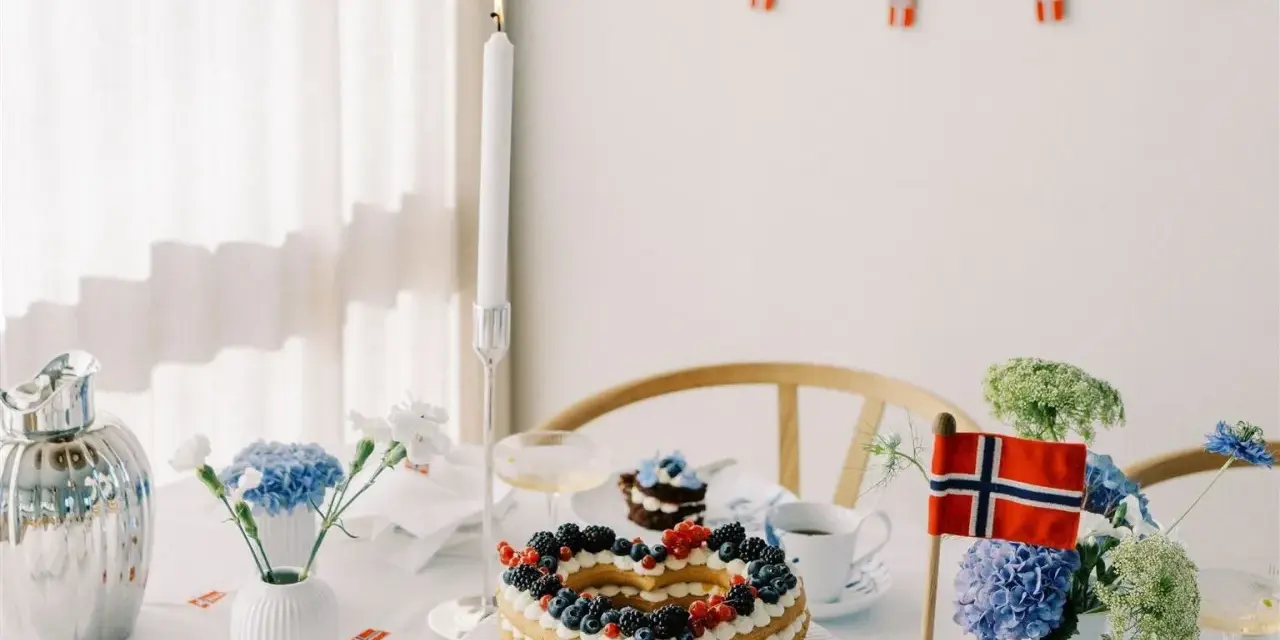 Festligt dukat bord med hjärtformad tårta, blommor och norska flaggor. Perfekt för firande med flaggor att skriva ut.