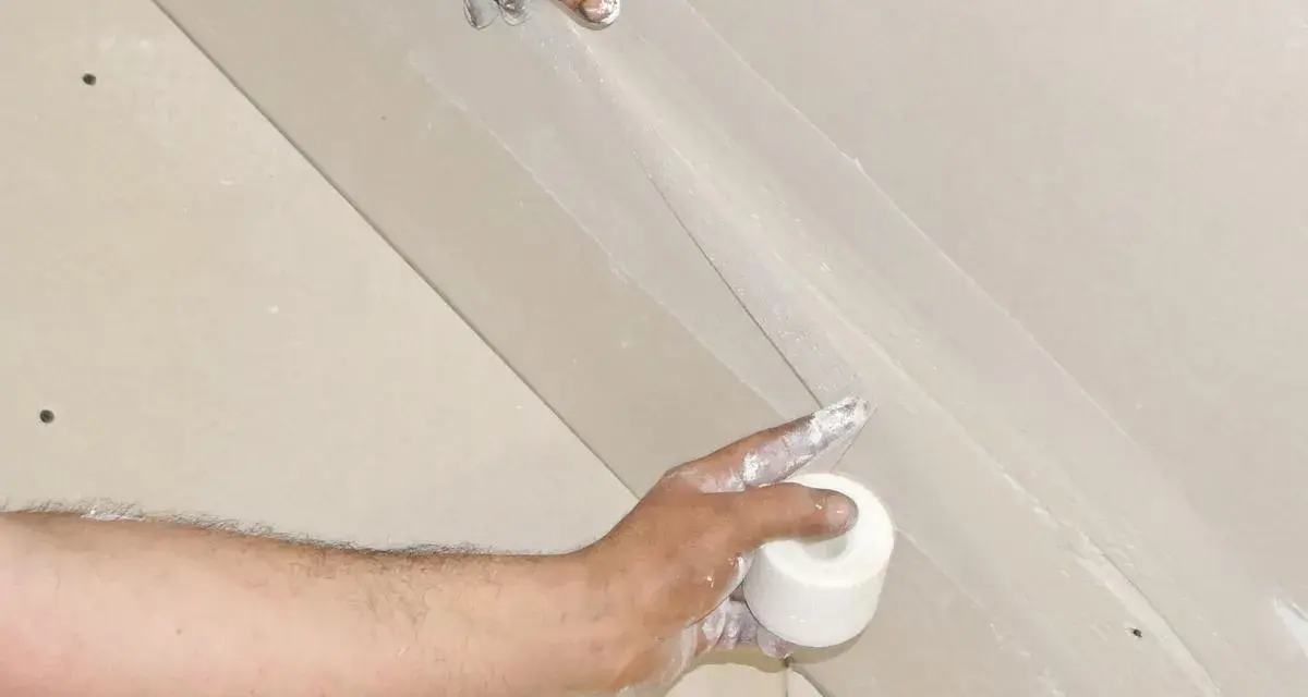 Hände arbeiten an einer q4 Spachtelung. Eine Rolle Klebeband wird gehalten, während die andere Hand die Spachtelmasse aufträgt.