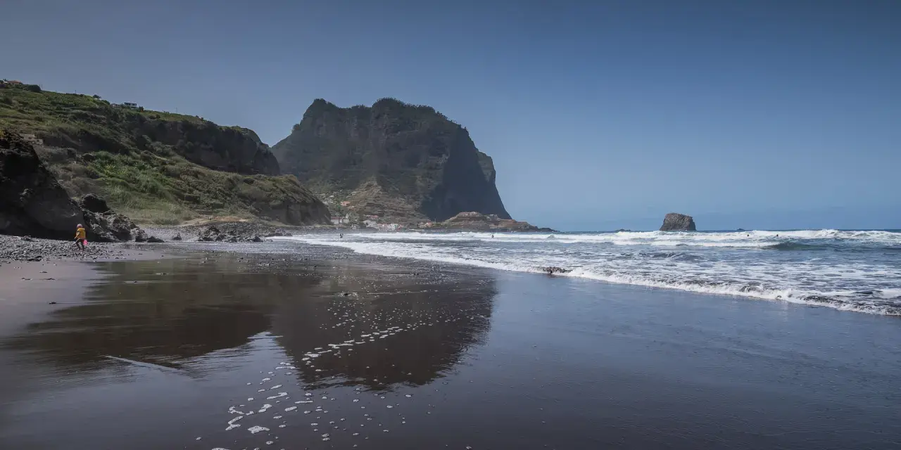 Dziecko bawi się na czarnej plaży Madera, w tle widać skaliste klify i ocean.