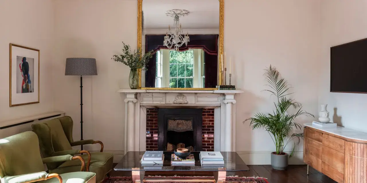 Sofá verde, chimenea con espejo dorado y candelabros. La sala de estar exhibe colores elegantes y un ambiente acogedor.