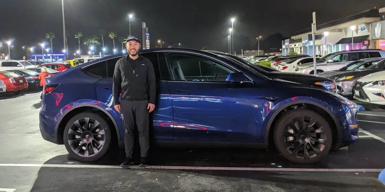 Mężczyzna stoi obok ciemnoniebieskiego Tesli Model Y na nocnym parkingu.