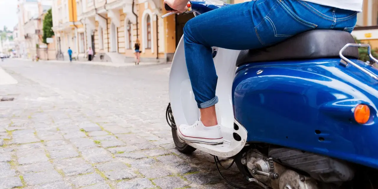 Un uomo in jeans guida uno scooter blu su un lastricato, un'immagine che evoca la libertà e lo spirito dell'art 52 cds.