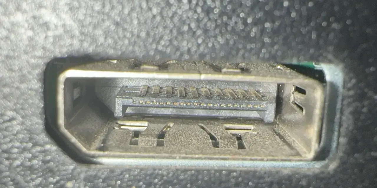 Närbild på ett dammigt displayport uttag med synliga kontakter och fästen.