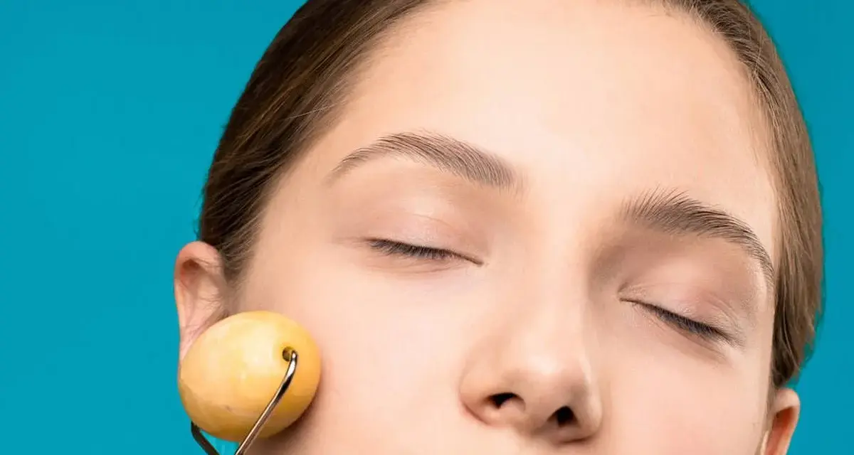 Mujer con ojos cerrados disfrutando de un masaje facial antienvejecimiento y drenaje con rodillo de jade.