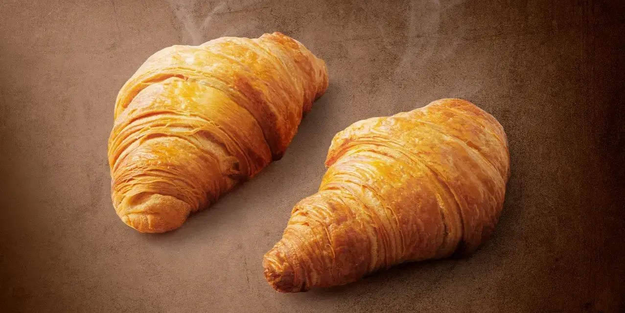 Dwa złociste croissanty z nadzieniem orzechowym z Lidla, parujące delikatnie. Idealne na śniadanie, zaspokoją głód i dostarczą energii.