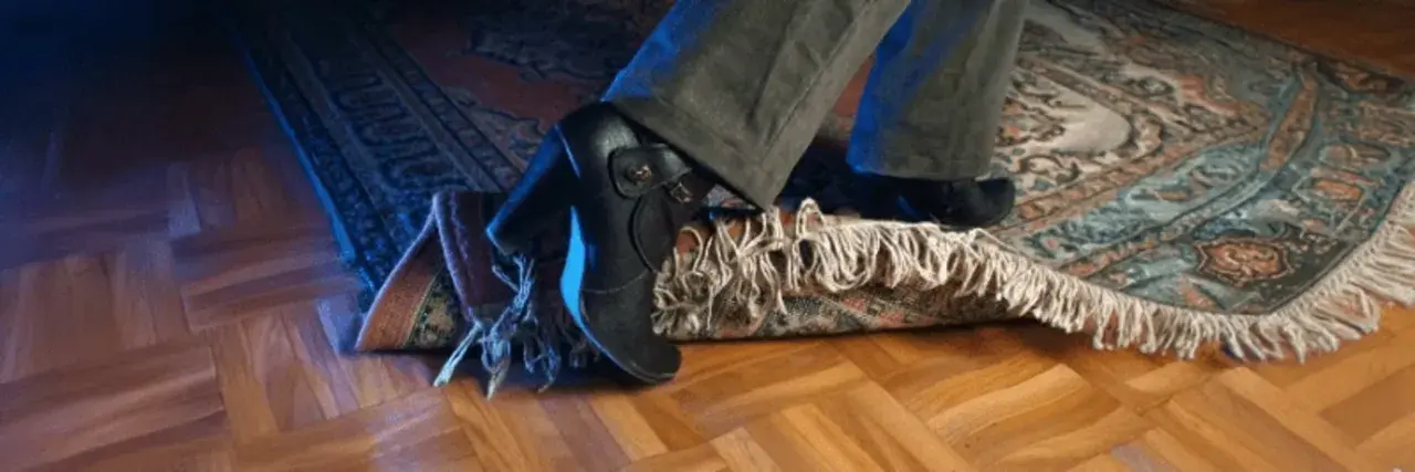 En fot med klacksko snubblar på en matta. En antiglidmatta hade kunnat förhindra detta.