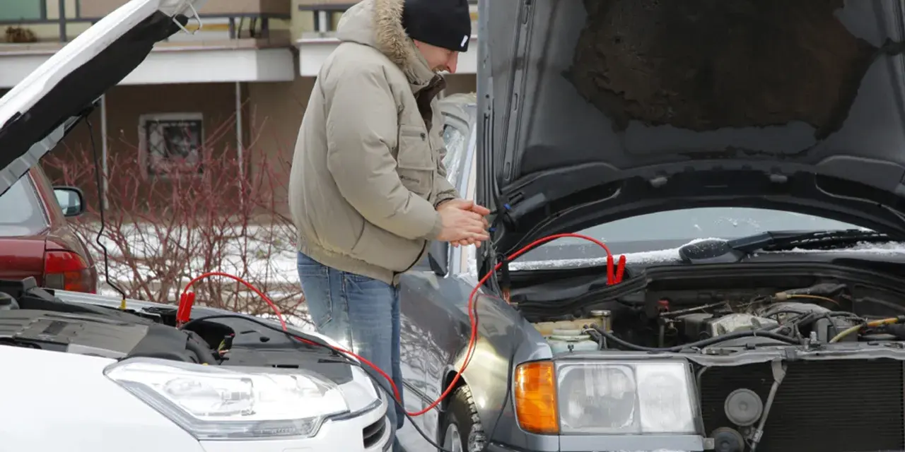 Mężczyzna podłącza kable rozruchowe do samochodu, by odpalić toyotę hybrydę na kable.