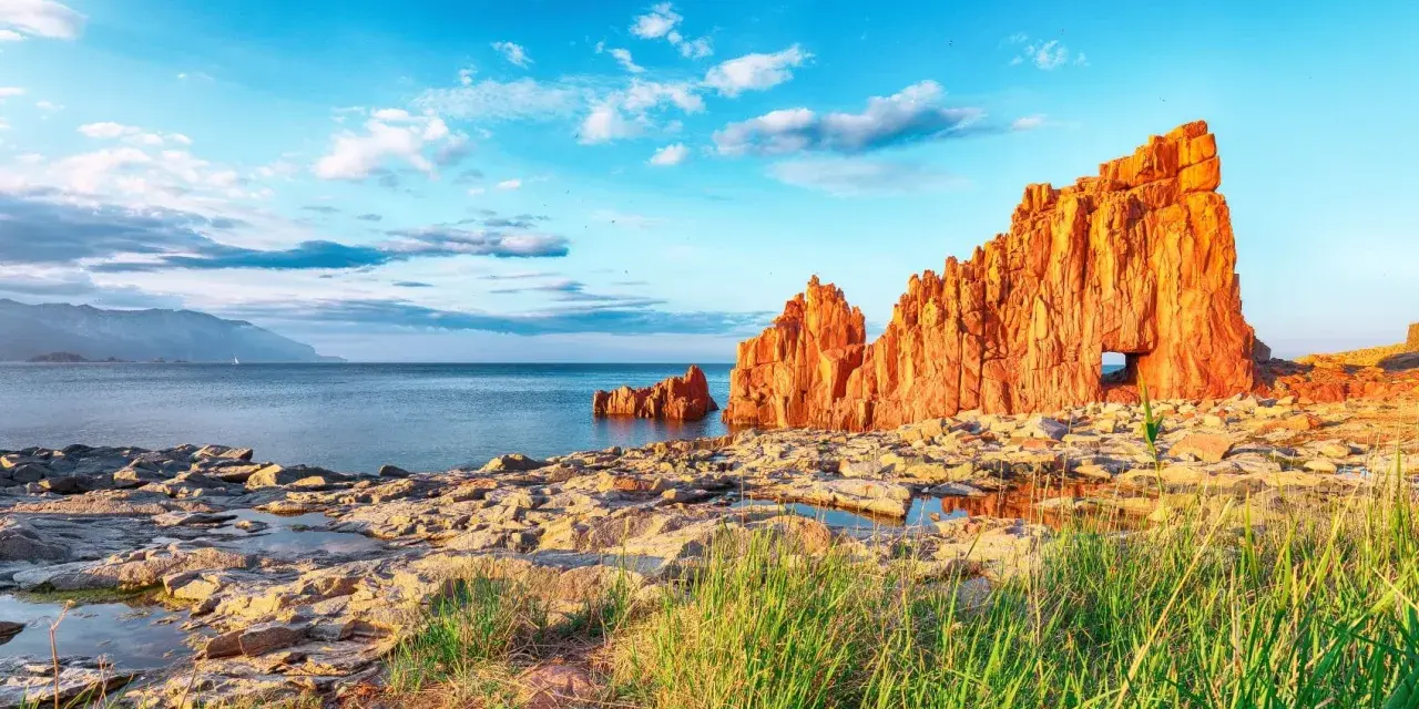 Scogliere rosse a picco sul mare blu, con un arco naturale, vicino ad Arbatax centro storico.