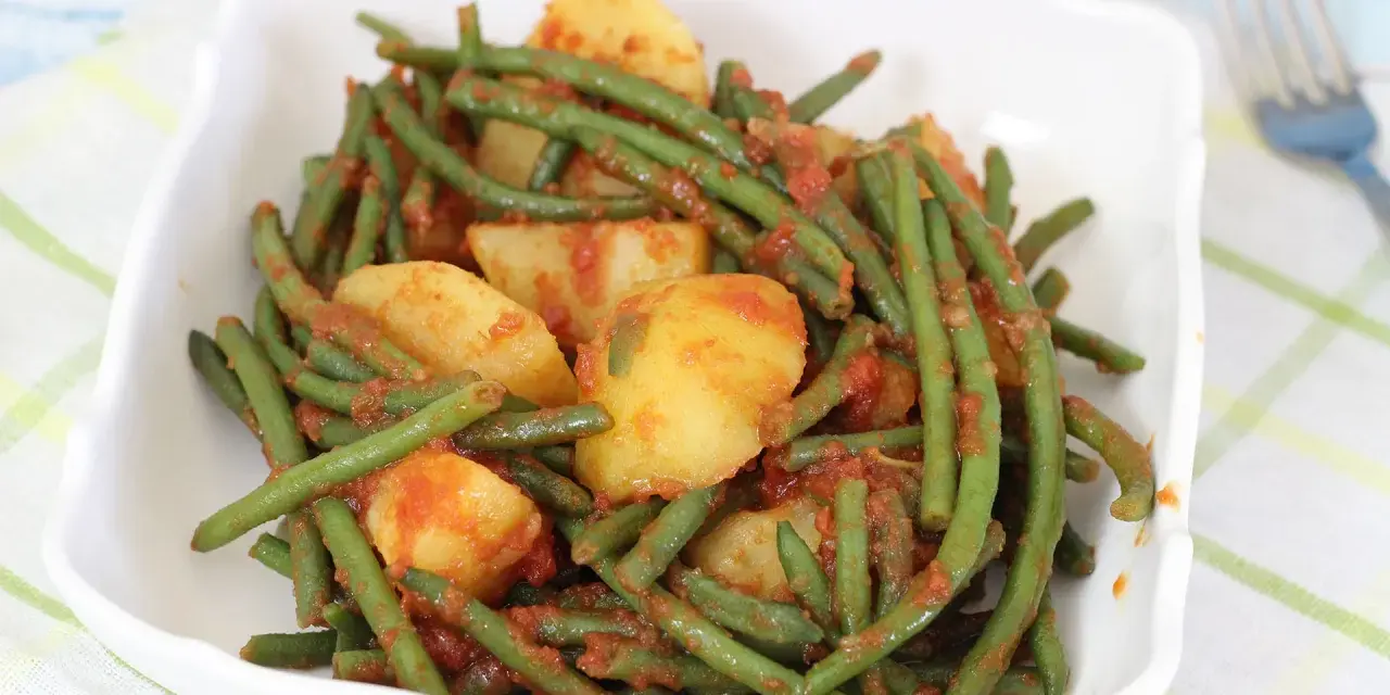 Fagiolini in umido con patate, un piatto saporito e colorato, servito in una ciotola bianca su una tovaglia a quadri.