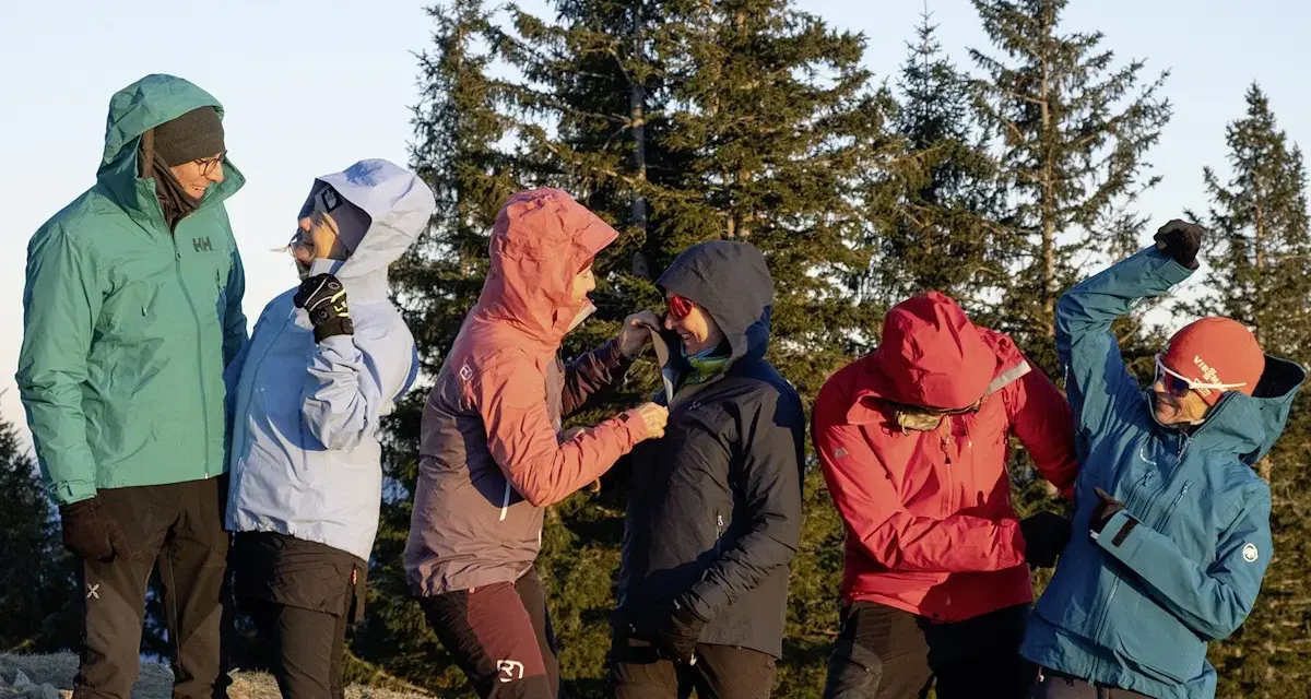 Sechs Personen in bunten Hardshelljacken stehen vor Bäumen. Eine Hardshelljacke schützt vor Wind und Wetter.
