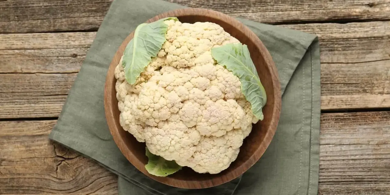 Ein frischer, ganzer Blumenkohl in einer Holzschale auf einem grünen Tuch. Perfekt, um blumenkohl roh essen als gesunden Snack.