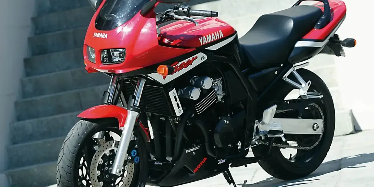 Czerwony motocykl Yamaha FZ6 z czarnym siedzeniem i owiewką, zaparkowany na zewnątrz.