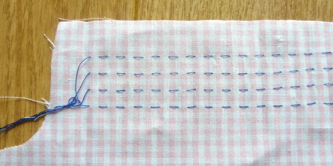 Tissu à carreaux rose et blanc avec des points de couture bleus, préparant un smock couture.