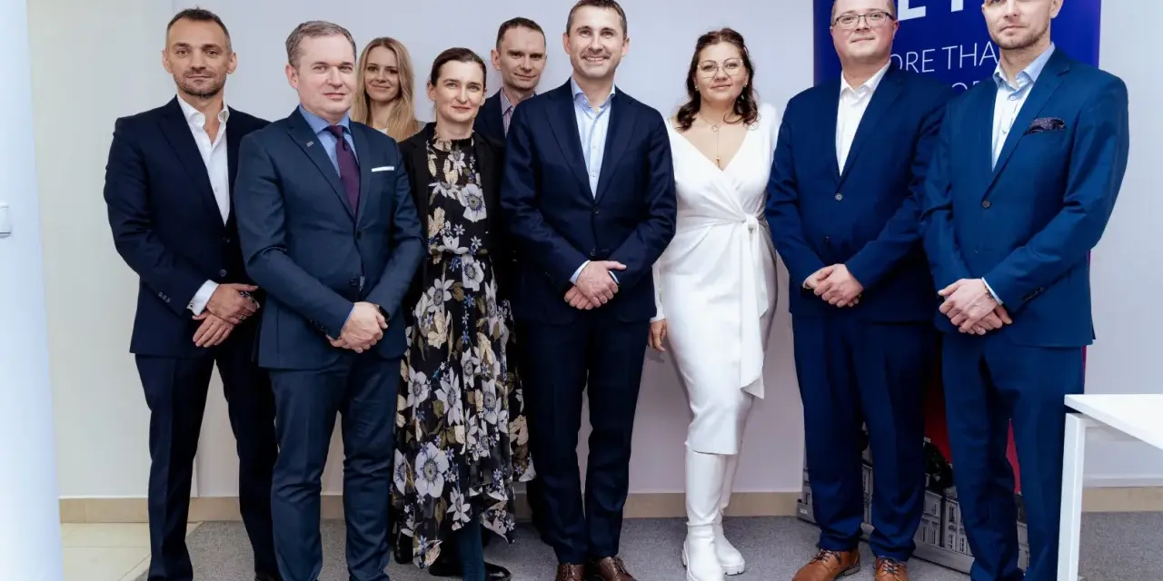 Grupa osób w garniturach i sukience pozuje do zdjęcia na tle banera.